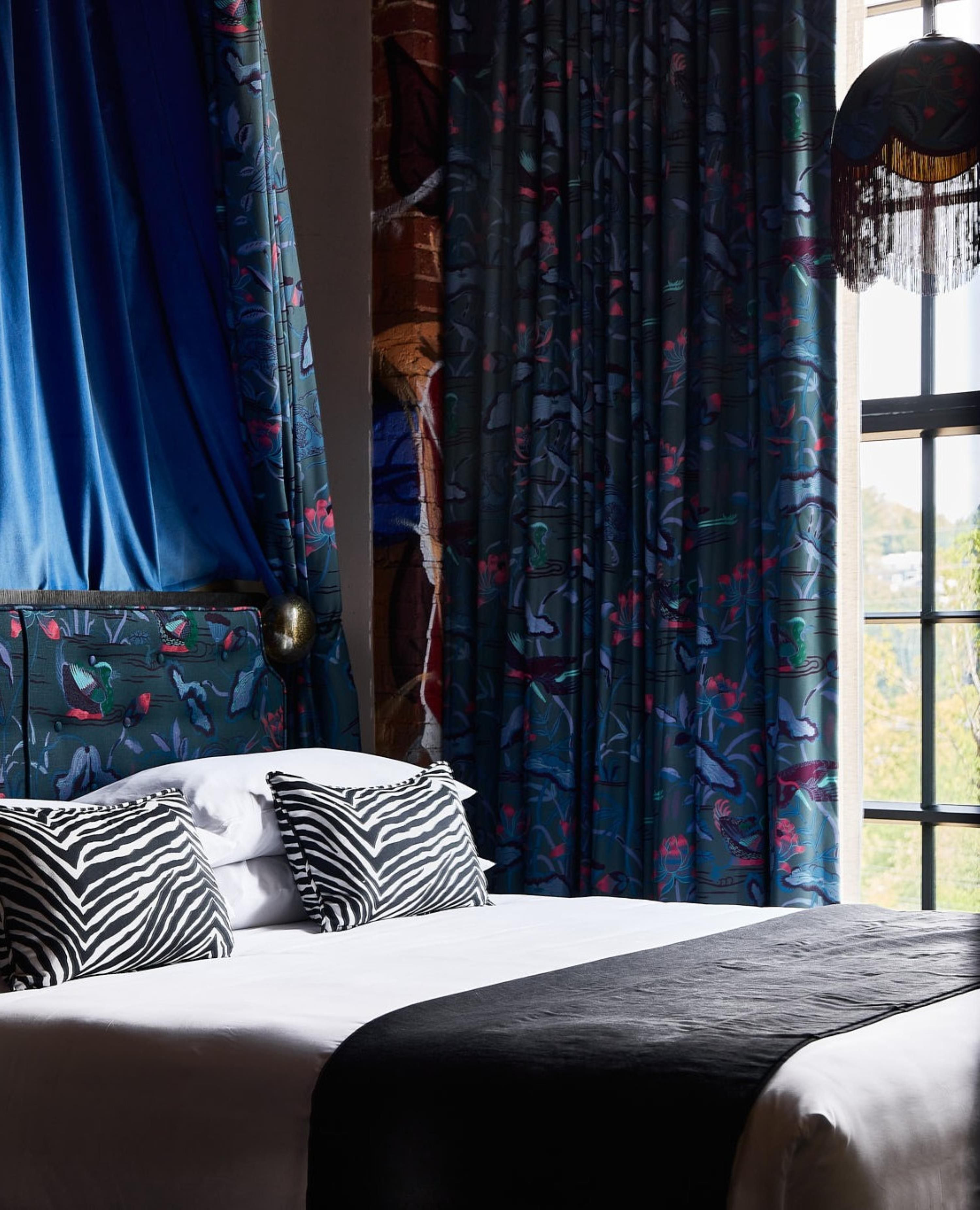 Une chambre à coucher avec un lit, des coussins à motifs zébrés et des rideaux ornés de motifs d’oiseaux.