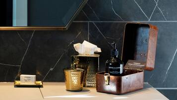 A bathroom vanity with a marble backsplash, a gold-colored container, a tissue box, and a leather case with a bottle.