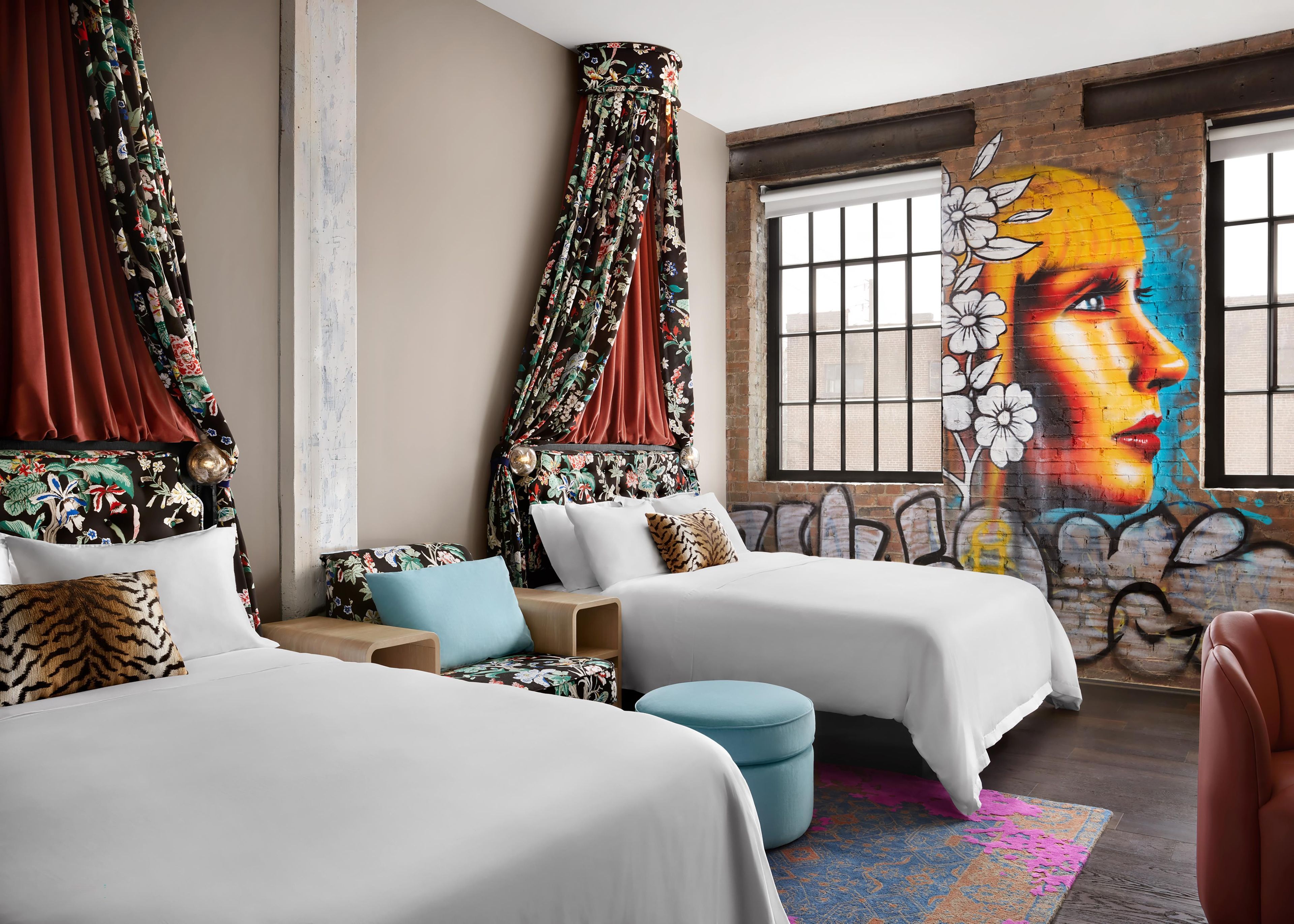 A hotel room with two beds, a colorful mural, and a large window.
