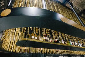 Baarissa on kaareva, musta baaritiski, ja sen päällä on esillä kultaketjuja ja erilaisia alkoholijuomapulloja.