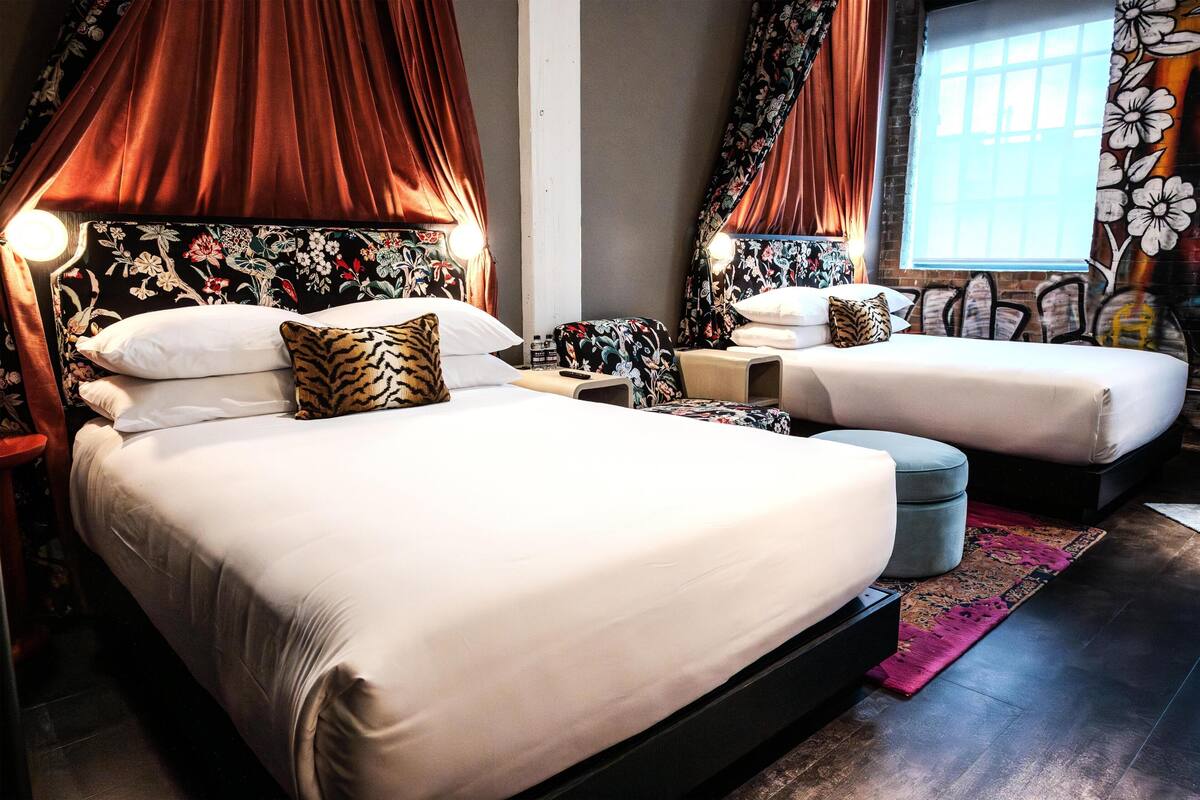 A hotel room with two beds, a large window, and a decorative curtain.