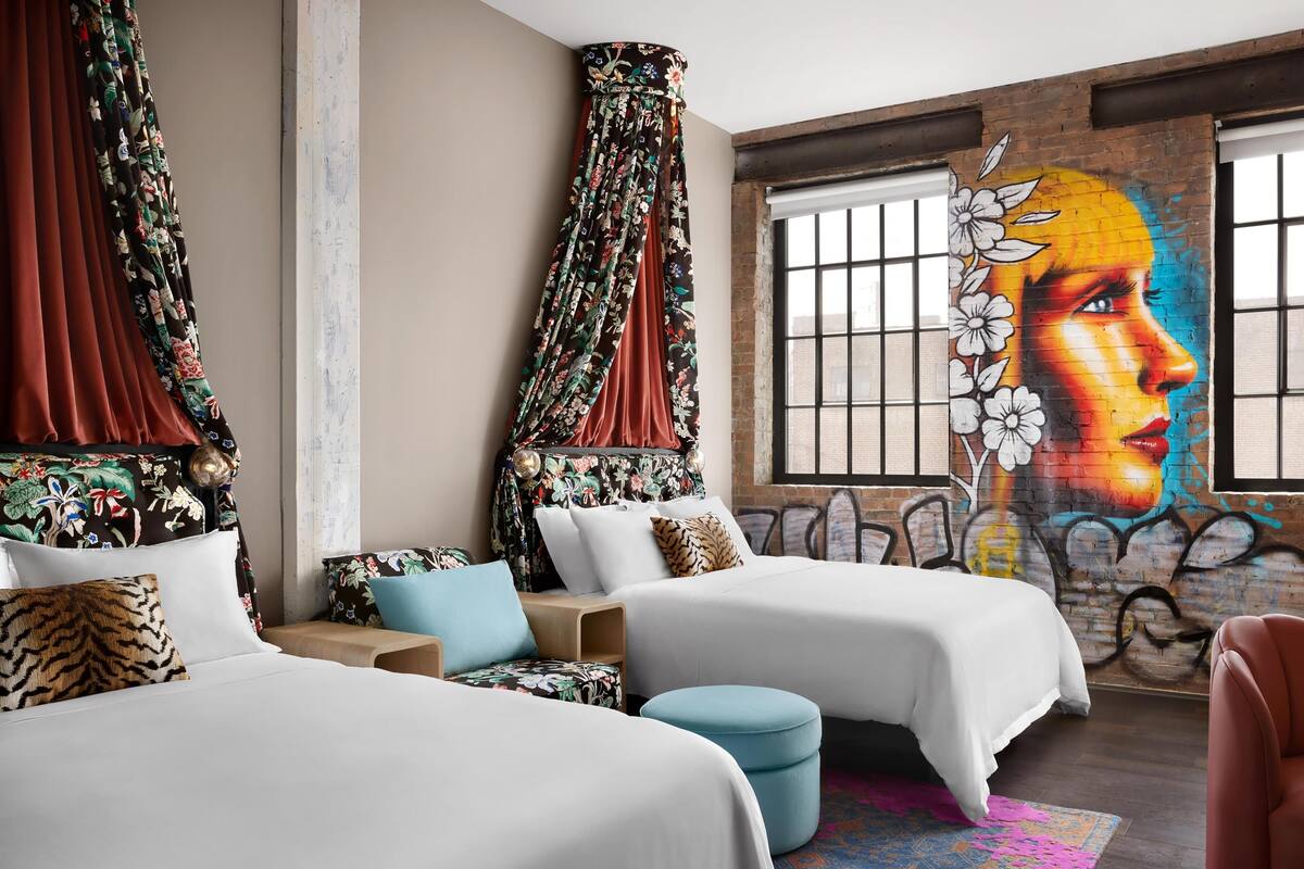 A hotel room with two beds, a mural on the wall, and a large window.