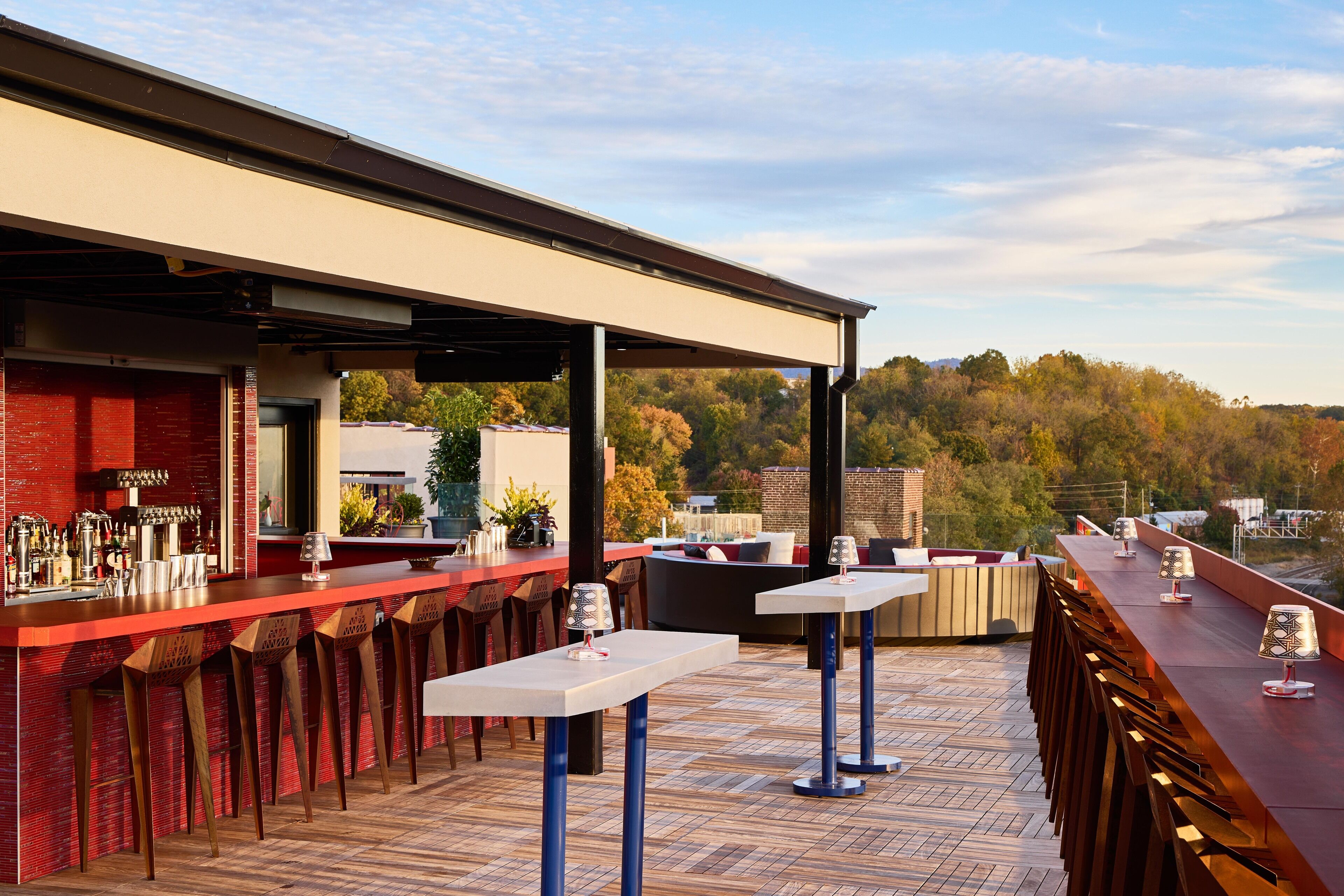 An outdoor bar area with multiple seating options, including bar stools and tables, and a view of the surrounding landscape.