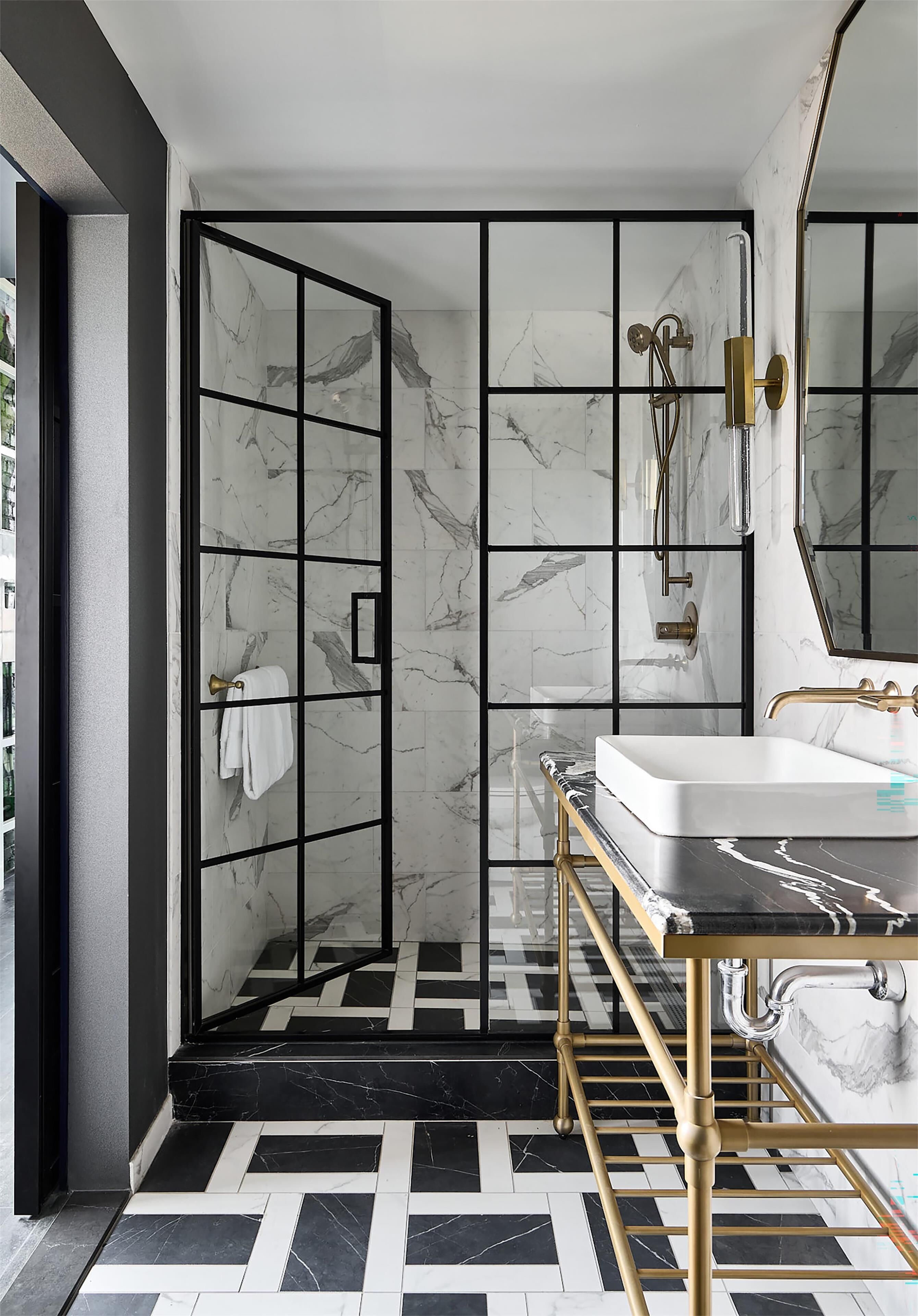Un baño moderno con cabina de ducha de vidrio, suelo de baldosas de mármol y tocador dorado con lavabo blanco.