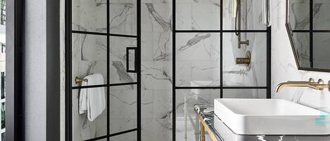 Un baño moderno con cabina de ducha de vidrio, suelo de baldosas de mármol y tocador dorado con lavabo blanco.