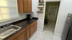 Cozinha com armários de madeira, bancada de granito, pia de aço inoxidável, ventilador de teto e geladeira.