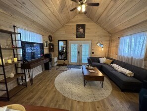 A cozy cabin-style room with a wooden interior, a ceiling fan, a large flat-screen TV, a sofa, and a coffee table.