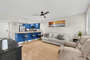 Ein modernes Wohnzimmer mit Sofa, Essbereich mit Bar und Küche mit blauen Schränken.