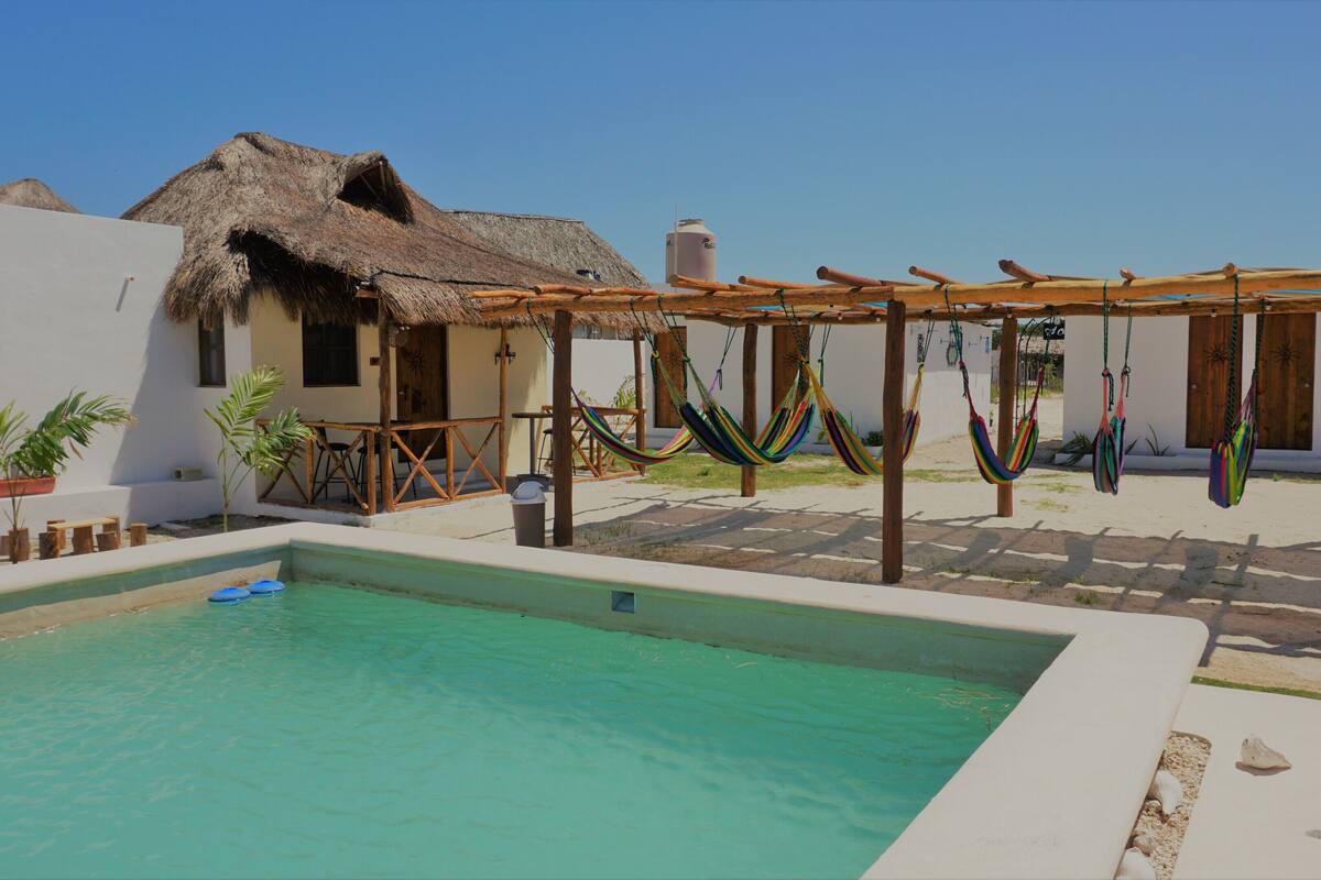 A pool area with a thatched-roof structure, hammocks, and a clear blue sky.
