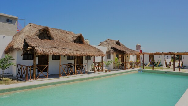 A poolside area with thatched-roof cottages, a clear sky, and a water tank in the background. - Casa Frida (Progreso)