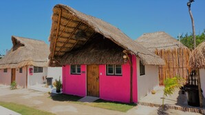 A row of thatched-roof cottages with pink walls and a central door. - Casa Frida (Progreso)