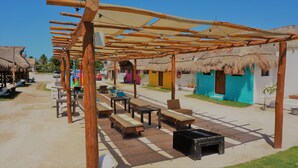 A covered outdoor seating area with wooden tables and benches, thatched-roof huts, and a clear sky. - Casa Frida (Progreso)