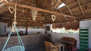 A rustic interior with a thatched roof, wicker furniture, and a stone wall. - Casa Frida (Progreso)