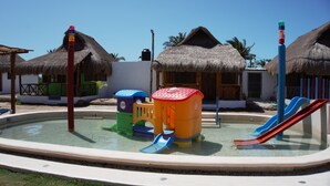 A pool area with slides and play structures, surrounded by thatched-roof buildings. - Casa Frida (Progreso)