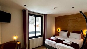 Een hotelkamer met een tweepersoonsbed, een bureau met stoel, een raam met gordijnen en een houten hoofdeinde.