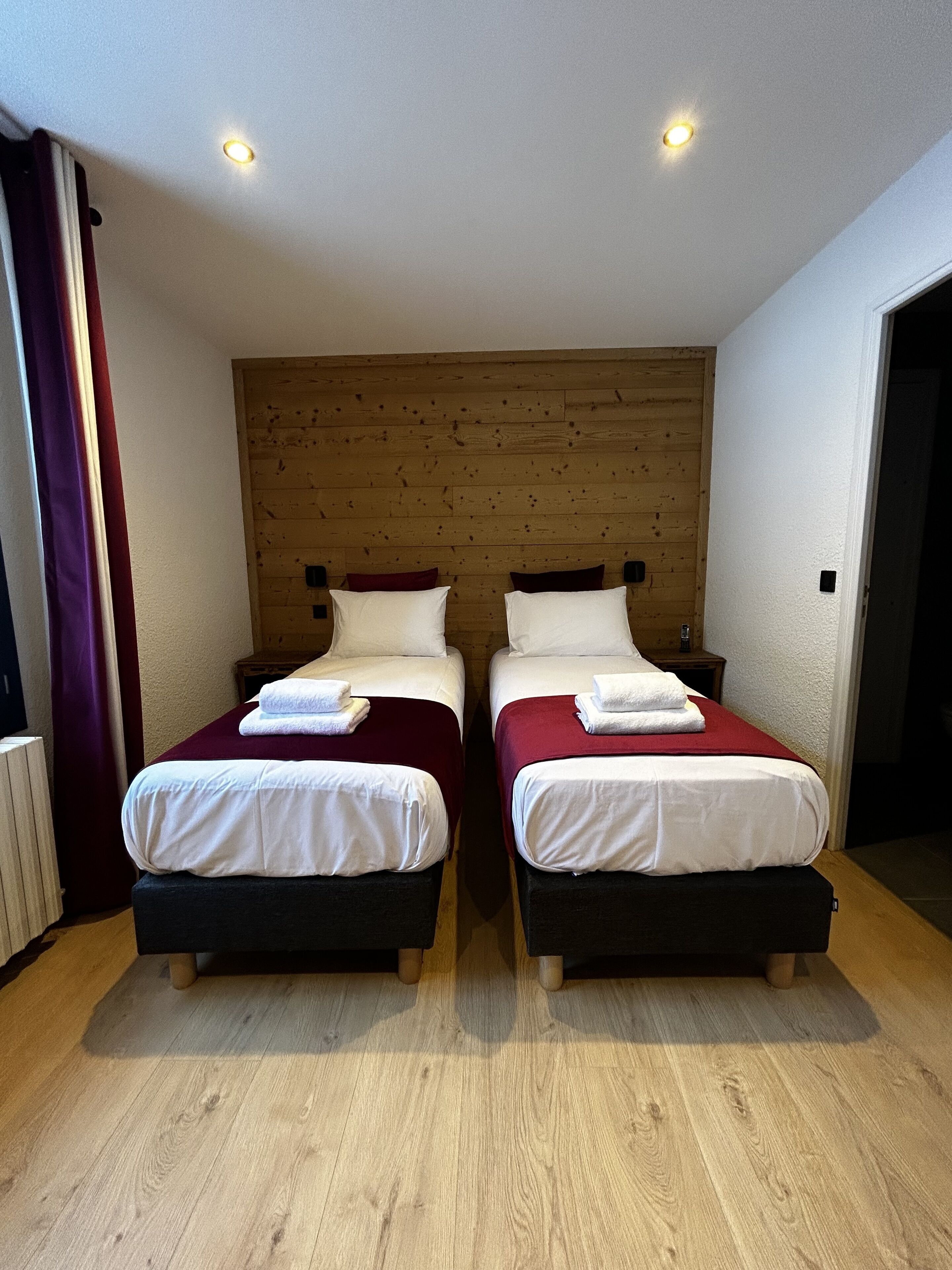 Quarto com duas camas, cabeceira de madeira, roupa de cama branca e chão de madeira.