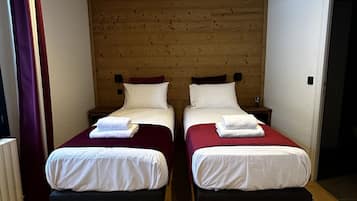 Quarto com duas camas, cabeceira de madeira, roupa de cama branca e chão de madeira.
