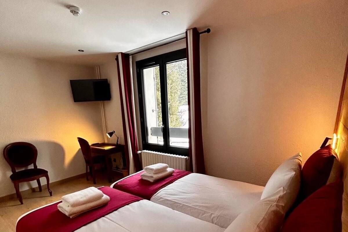 Una habitación de hotel con una cama grande, un escritorio con silla, un televisor montado en la pared y una ventana con cortinas.