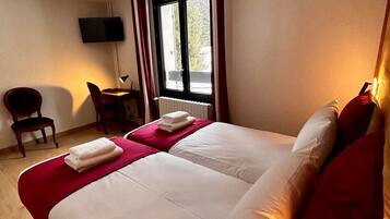 Ein Hotelzimmer mit einem großen Bett, einem Schreibtisch mit Stuhl, einem an der Wand montierten Fernseher und einem Fenster mit Vorhängen.