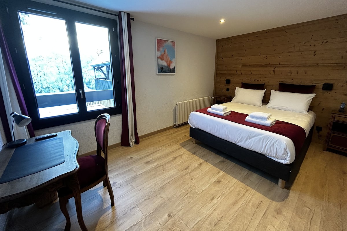 Un dormitorio con cabecera de madera, cama grande con ropa blanca, escritorio con silla y ventana con cortinas.