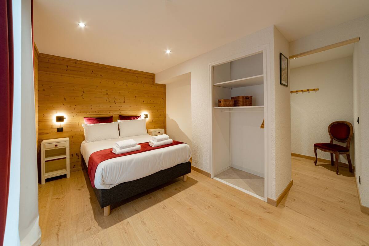 Un dormitorio con cabecera de madera, cama con ropa de cama blanca, mesita de noche, armario y una silla.