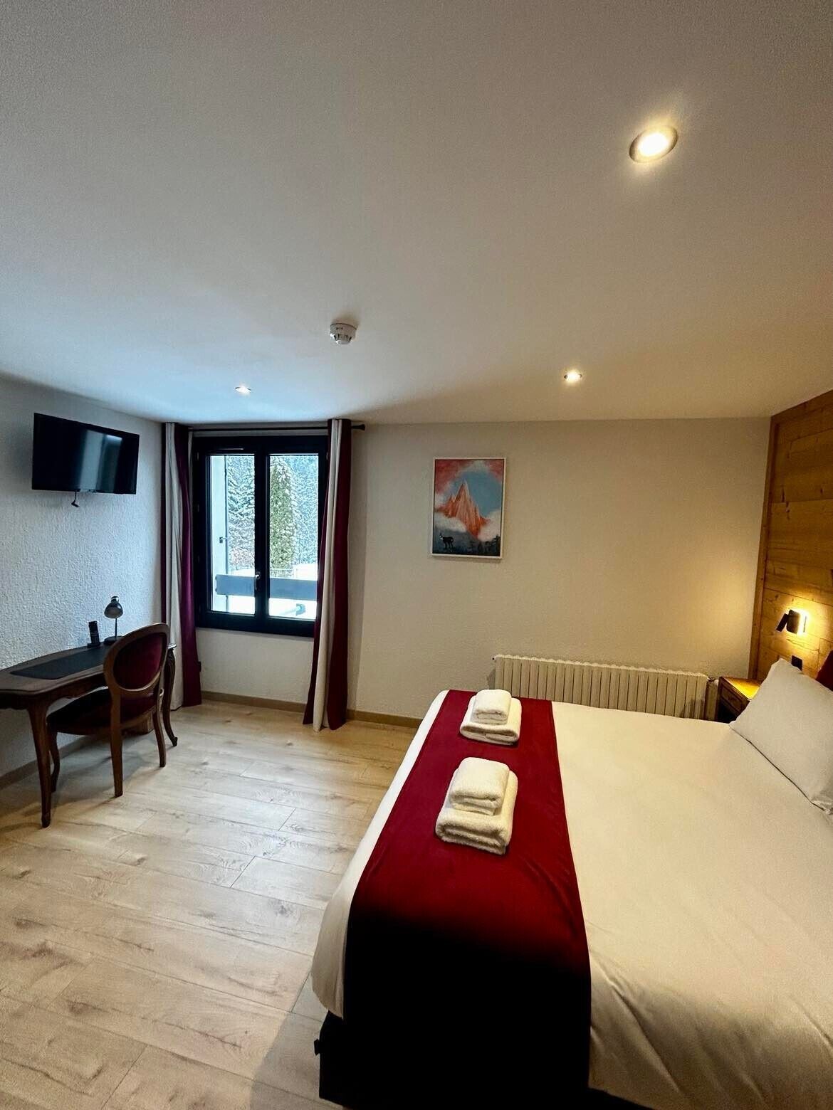 Habitación de hotel con cama, escritorio, silla, televisión y ventana con cortinas.