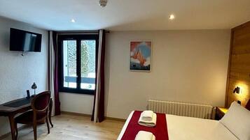 Habitación de hotel con cama, escritorio, silla, televisión y ventana con cortinas.