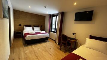 Habitación de hotel con una cama grande, una cama más pequeña, un escritorio con silla, televisor montado en la pared y una ventana con cortinas.