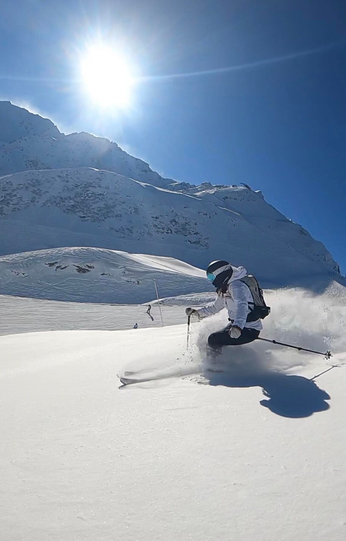 Iemand skiënd op een besneeuwde helling, met een heldere lucht en een berg op de achtergrond.