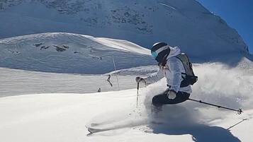 Iemand skiënd op een besneeuwde helling, met een heldere lucht en een berg op de achtergrond.