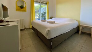 A bedroom with a bed, a desk with a computer, a mirror, and a window with curtains. - Escapade au Soleil – T3 jardin dans résidence avec  accès direct plage (Le Grau-du-Roi)