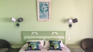 A bedroom with a green headboard, two white pillows, two tropical summer-themed pillows, a framed picture of a palm tree, and two wall-mounted lamps. - Guadeloupe, Saint-François Anse des Rochers, 1/4 villa , vue mer citerne wifi pr (Saint-François)