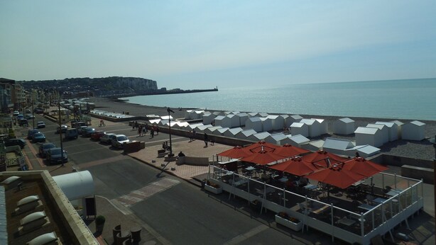 A coastal area with a beach, a promenade, and a row of white tents with red roofs, likely for accommodation or events.