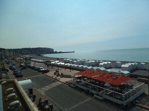Zona costera con playa, paseo marítimo y una hilera de carpas blancas con techos rojos, posiblemente para alojamiento o eventos.