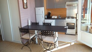 A compact kitchen with a dining table, four chairs, a chandelier, a refrigerator, a stove, and a sink.