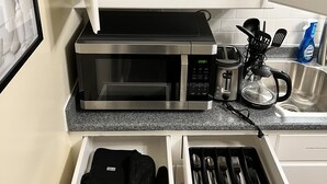 A kitchen with a microwave, toaster, and sink. There are white cabinets above and below the counter, and a drawer with utensils. - EKO Stay - Your Home Away From Home (Wauwatosa)
