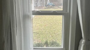 A room with a window, curtains, and a view of a yard with trees and a house. - EKO Stay - Your Home Away From Home (Wauwatosa)