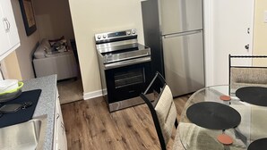 A compact kitchen with a built-in oven, a refrigerator, and a dining area with a glass table and chairs. - EKO Stay - Your Home Away From Home (Wauwatosa)