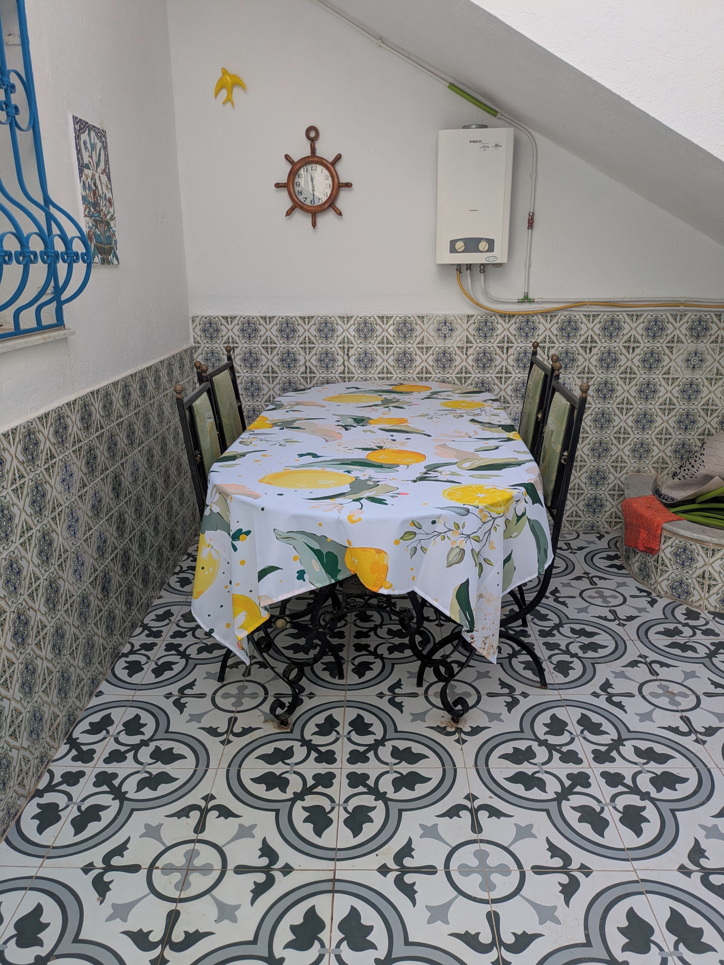 A dining area with a table covered by a floral tablecloth, surrounded by patterned tiles.