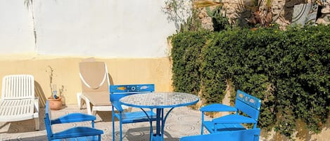 A patio with blue metal chairs and a round table, surrounded by patterned tiles.