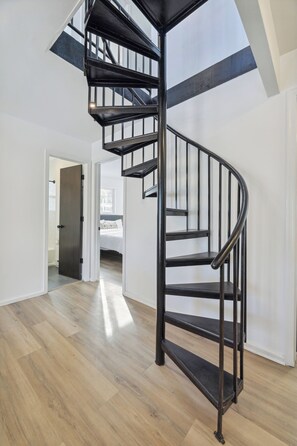 Eine moderne Wendeltreppe mit schwarzen Metallgeländern in einem hellen, offenen Wohnbereich mit Holzboden.