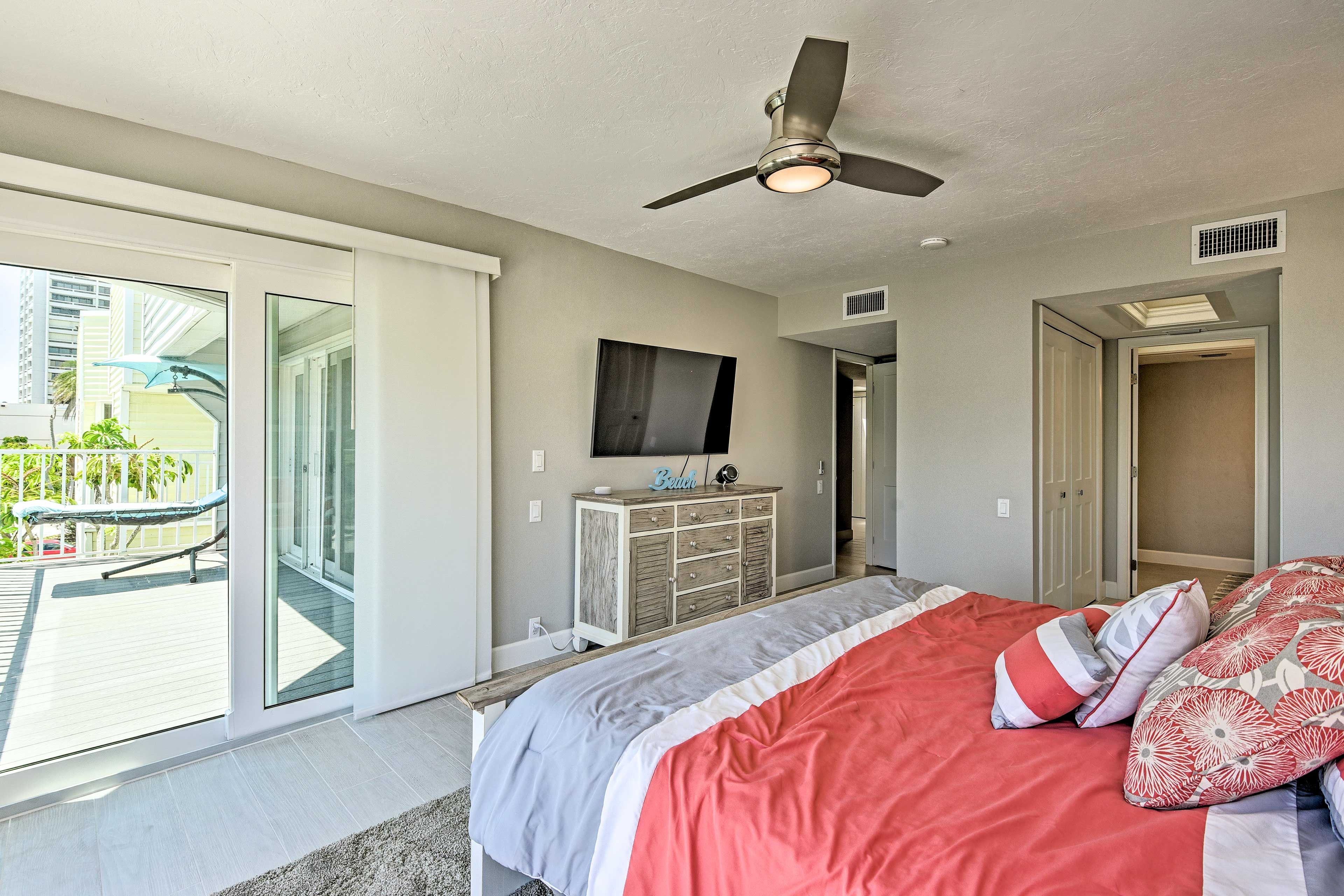 A bedroom with a bed, a ceiling fan, a TV, a dresser, and a sliding glass door to a balcony.