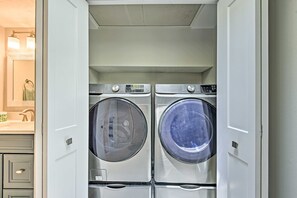A laundry room with two front-loading washing machines and a mirror above them. - Coastal Surfside Swank by Beachside Management (Siesta Key)