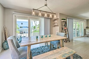 A dining area with a wooden table, chairs, and a bench. There is a chandelier above the table and a blue rug on the floor. - Coastal Surfside Swank by Beachside Management (Siesta Key)