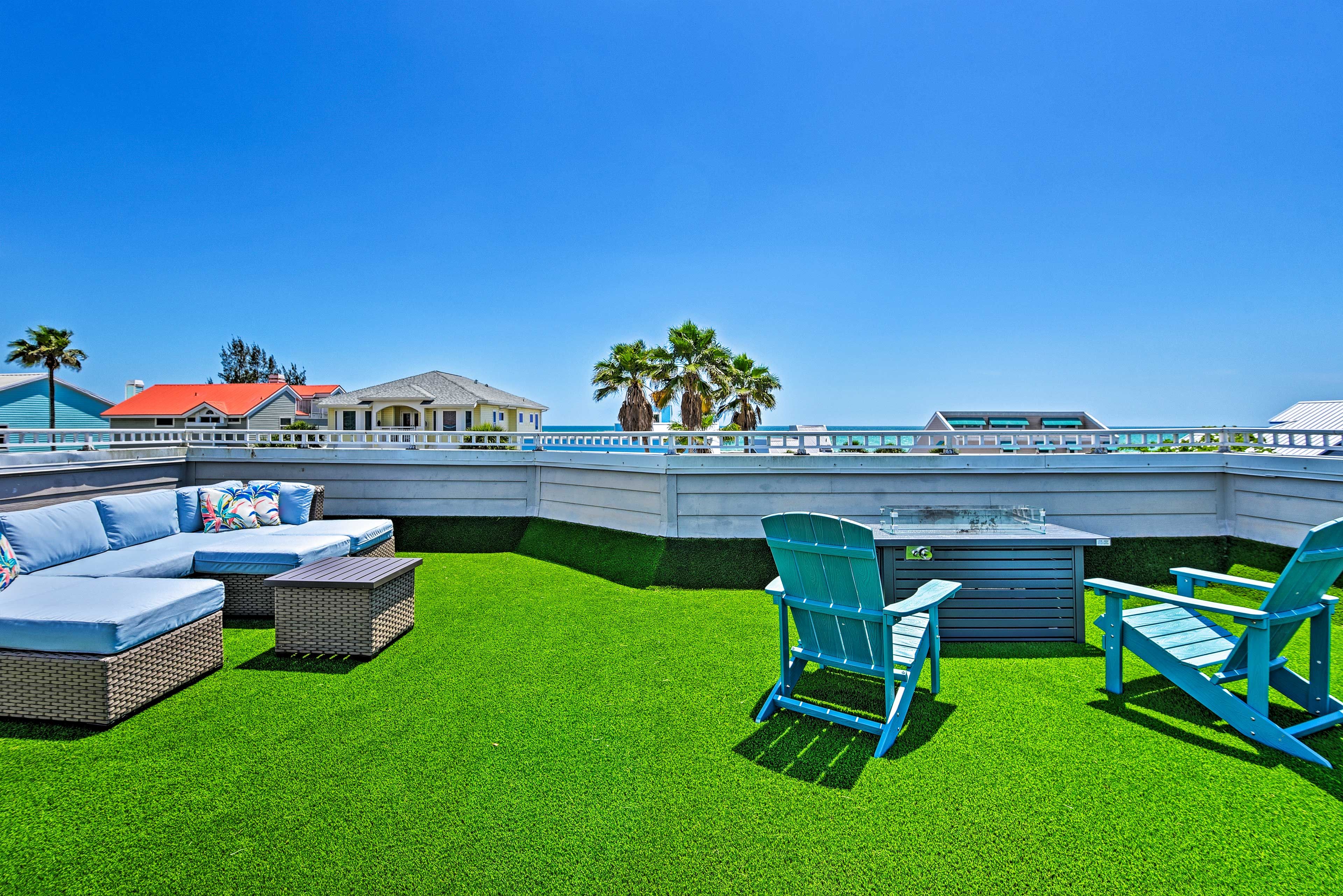 An outdoor patio with a sectional sofa, two blue Adirondack chairs, and a small table.