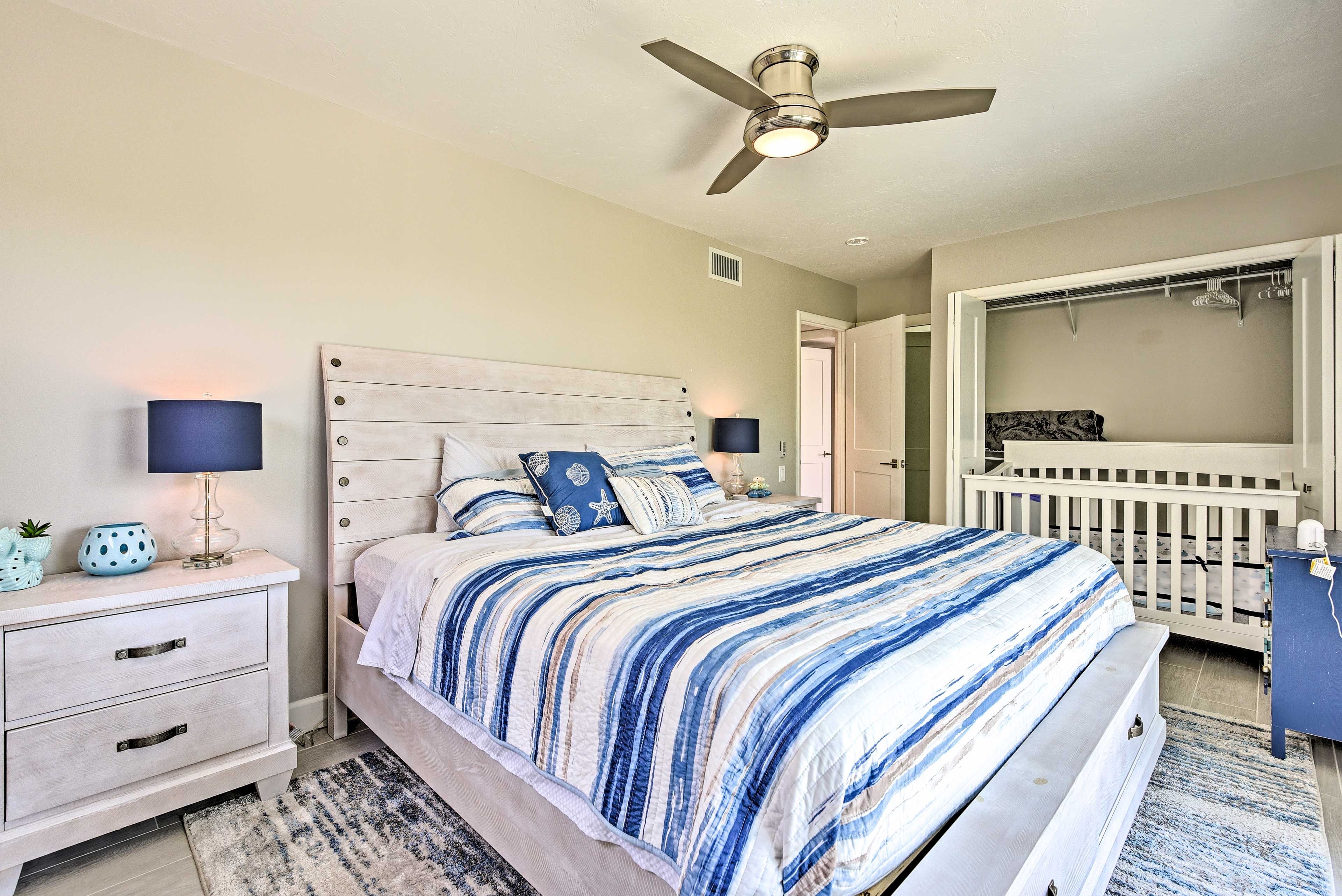 Ein Schlafzimmer mit einem Bett, Nachttischen, einem Deckenventilator, einem begehbaren Kleiderschrank und einem Babybett.