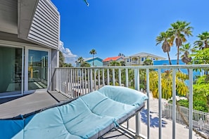A balcony with a cushioned seating area, a pool, and a view of neighboring houses and palm trees. - Coastal Surfside Swank by Beachside Management (Siesta Key)