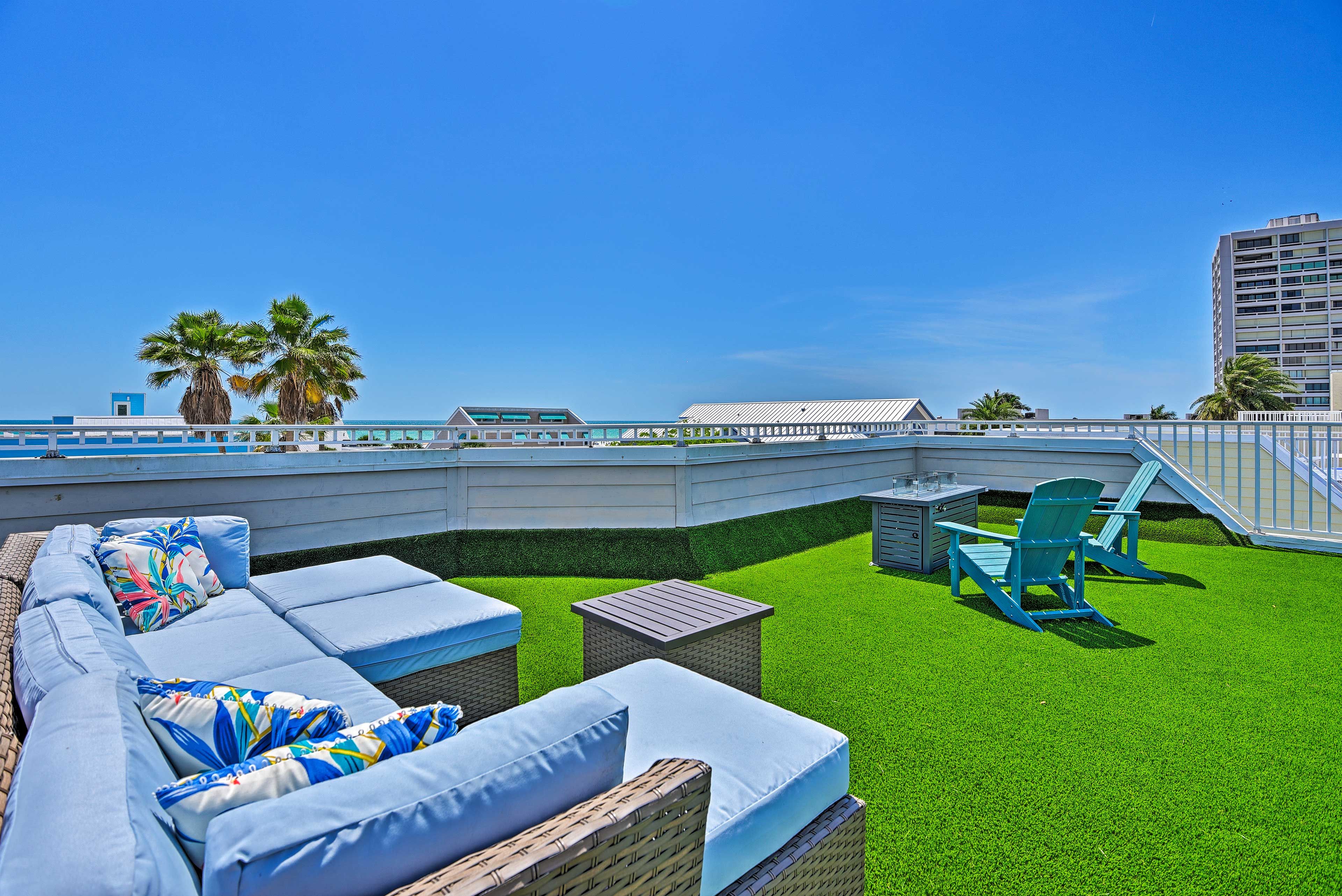 A rooftop terrace with a green lawn, wicker furniture, and a view of the city skyline.