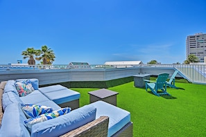 A rooftop terrace with a green lawn, wicker furniture, and a view of the city skyline. - Coastal Surfside Swank by Beachside Management (Siesta Key)