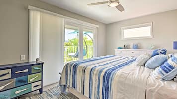 Un dormitorio con cama, cómoda, ventilador de techo y ventana con vista a un balcón.